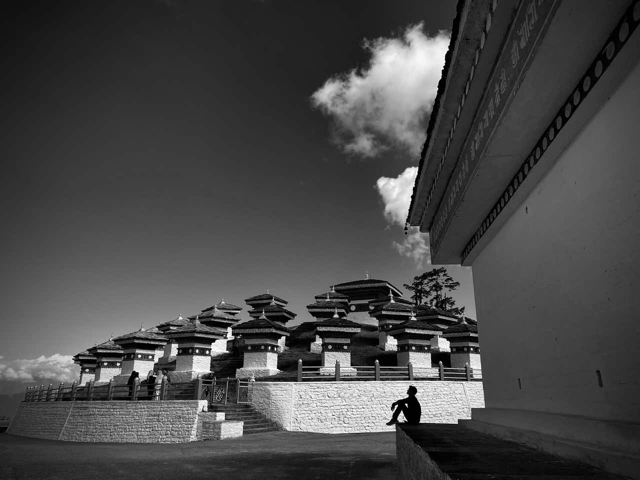 A beautiful black and while image of the stupas atop Bhutans Dochu La pass with the sillhouette of a sitting man in the forground