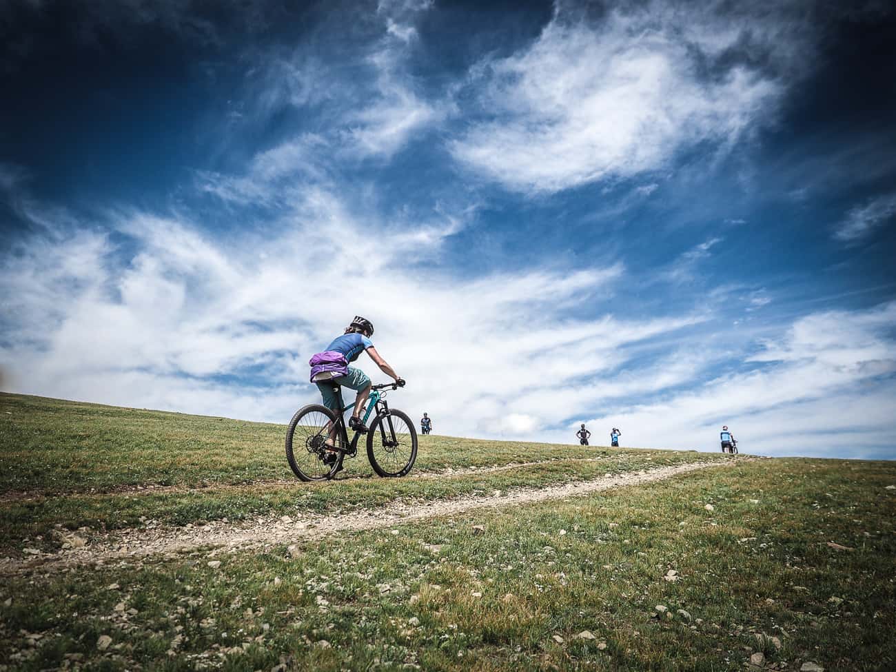 cyclists in Mongolia riding a gravel track up hill beneath a blue sky