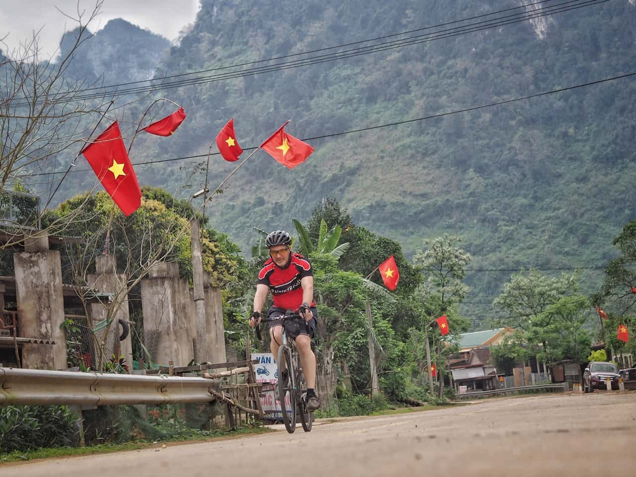 cyclist touring vietnam beneath vietnamese flags