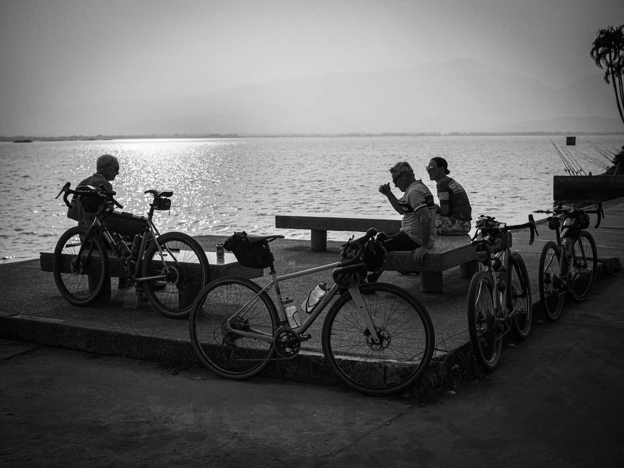 black and white image of gravel cyclists resting by a lake during Thailand bike packing ride